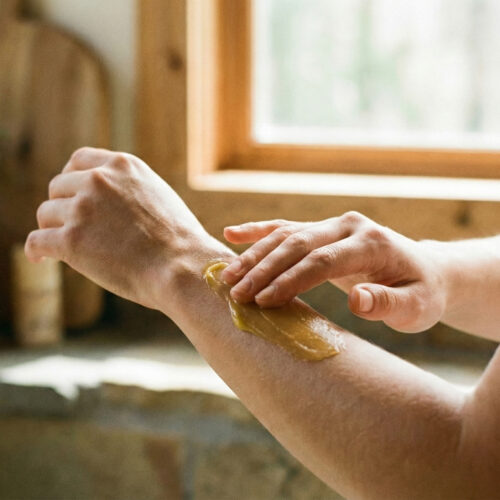 eckco-barrier-balm-application-sensitive-skin-ritual Close-up applying Eckco natural barrier balm to the forearm to soothe sensitive skin, highlighting the rich golden texture in a calm, natural setting.
